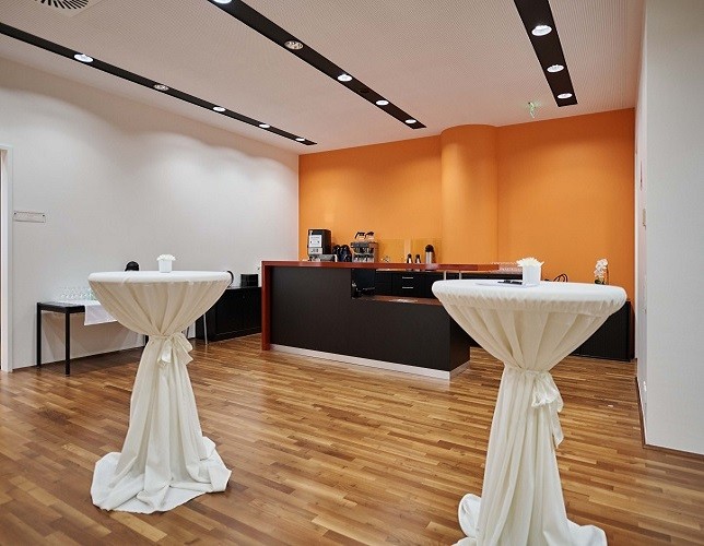 Foyer Konferenzbereich mit Parkettboden weiße-orangen Wänden Theke und zwei Stehtischen