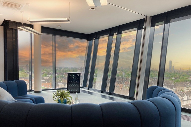 Arcadia Park Innenansicht großer Präsentationsraum mit blauem Sofa, Glaskühlschrank mit Getränken und Panorama-Blick auf Düsseldorf